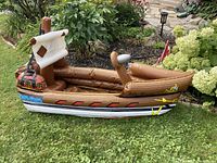 Side view of the brown inflatable pirate ship resting on grass with wood grain print and red and blue decorative accents, showing the inside seating area and part of the sail structure removed.