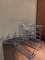 Photo showing all metal racks arranged on a wooden table, including one organizer rack, five door racks, and kitchen cupboard organizers in plastic packaging.
