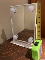 Front view of rectangular vanity mirror with four light bulbs at each corner and a white stand, tape measure showing height.