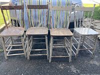 Front view of four white antique wooden chairs with visible stripped paint and wired reinforcement beneath seats
