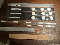 Four black metal magnetic strips with attached cream-colored round magnets, one silver metal strip, and several smaller metal pieces on a wooden surface.