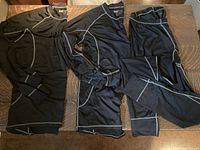 Two black Alizee long sleeve shirts and one pair of matching pants with grey seam detailing, laid flat