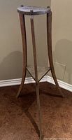 Photo of tall wooden plant stand with round top and triangular lower shelf showing wood condition and leg spacing
