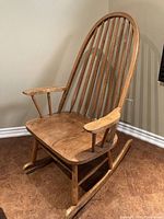 Front-side view of solid oak rocking chair showing high spindle back, armrests, and contoured wooden seat.