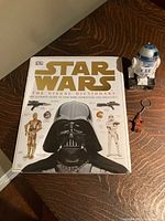 Photo showing Star Wars Visual Dictionary book closed with R2-D2 candy dispenser and Chewbacca key chain beside it.