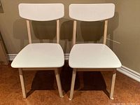 Front view of two white Scandinavian-style chairs placed side by side showing white seat and backrest with natural wood legs