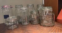 Nine hinged glass mason jars with metal clasp lids on a wood surface, showing various sizes and shapes.