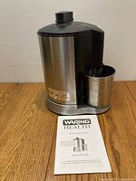 Waring juice extractor front view with manual placed in front showing model and brand