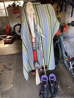 Rossignol skis with binding, ski poles, and ski boots set up against a striped multicolor fabric in a garage.