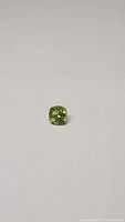 Apple green Peridot gemstone placed on a flat surface, showing cushion cut shape and color.