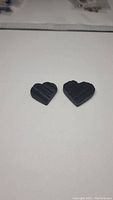 Two black heart-shaped tourmaline carvings displayed on a white surface showing size difference and carved texture.