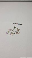 Photo of assorted small round diamond cut natural rainbow tourmaline gemstones scattered on a white background, showing various colors and clarity.