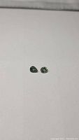 Two small green sapphires, oval and pear cut, laid on a white background, showing size and color.