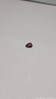Close-up photo of a polished pear-shaped cherry red almandine garnet gemstone on a white background, showing the color and transparency.