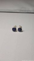 Front view of pair of small stud earrings with dark blue opaque round sapphire stones set in sterling silver bezels.