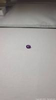 Oval cut natural amethyst gemstone resting on a flat surface, showing its strong purple color and size.
