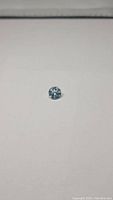 Close-up photo of a round brilliant cut natural sky blue topaz gemstone on a white background, showing the color and facets.