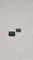 Two natural green tourmaline baguette cut gemstones on neutral background showing size and color variations