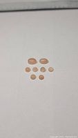 Nine natural peach moonstone cabochons arranged on a white surface, showing size and shape variety.