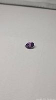 Natural pear cut purple amethyst gemstone on white background showing front and side facets.
