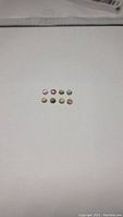 Top-down view showing eight small round cabochon rainbow tourmaline gemstones arranged in two rows on a white background.