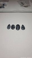 Four polished snowflake obsidian cabochons laid side by side on a white background, showing pear and oval shapes and snowflake inclusions.