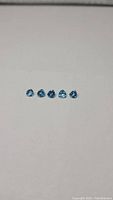 Five small heart shaped blue gemstones arranged in a row on a light background
