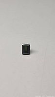 Rectangular baguette cut olive green tourmaline gemstone photographed against a plain background showing overall shape and color.