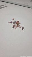 Multiple small natural tourmaline crystals in various colors and rough shapes, displayed on a white surface.