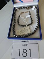 Blue box with black pearl necklace and matching bracelet inside. Necklace is a strand of 67 black pearls with three small Swarovski crystal hoops in the front. Bracelet is a 6mm black pearl strand of 29 pearls with adjustable clasp. Includes a Swarovski Elements tag.