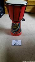 Full view of the 6-inch red djembe drum showing white drumhead, black ropes, and colorful patterned body in African style.
