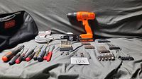 Photo showing all items laid out: Black & Decker cordless drill, small screwdrivers, multiple trays of screwdriver bits and attachments, 15 ft coaxial cable in original packaging, and carry bag.