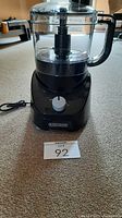 Front view of Black & Decker food processor showing black base with single dial control knob and clear plastic bowl with handle, power cord visible on left side.