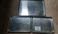 Three rectangular stainless steel baking sheets laid out on the floor, one large above two smaller ones, showing surface scratches.