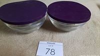 Top view of two glass prep bowls with purple silicone covers on top, placed on beige surface.