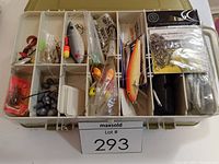 Top view of a plastic multi-compartment tackle box open, showing assorted fishing lures, hooks, sinkers, and bobbers organized in compartments.