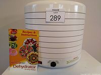 Closed white NESCO dehydrator with 5 stacked trays and recipe book displayed on the front side