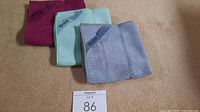 Three folded Norwex Enviro microfiber cloths in burgundy, mint green, and grey laid on carpet.