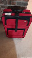 Front view of red suitcase showing two front zippered compartments and strap.
