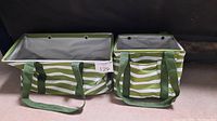 Two green and white striped utility totes, large rectangular tote on left and smaller square tote on right, displayed against dark background