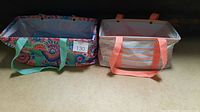 Two large utility totes side by side; one with kaleidoscope floral pattern, green handles, the other with colored lines pattern, pink handles.