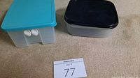 Two plastic food storage containers on carpet, blue lid rectangular and black lid square shape shown from top and side