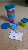 Six Tupperware snack cups with lids in varying colors stacked and displayed with two lids apart from cups.