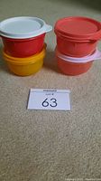 Set of four colorful snack bowls with lids arranged on carpet, visible colors red, yellow, coral, with white, yellow, and pink lids