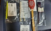 Image showing four kitchen tools still sealed in original packaging: yellow citrus peeler, red batter spoon, pair of toaster tongs, and Epicure baster.