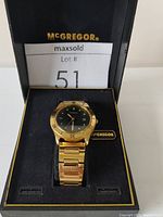 Vintage men's gold-toned McGregor wristwatch in black presentation box with visible branded tag, showing watch face and linked bracelet.
