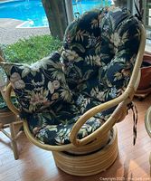 Front view of rattan swivel chair with tropical floral tufted cushion showing swivel base and cushion condition