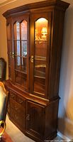 Front and side view of solid cherry wood hutch and china cabinet showing glass doors, brass hardware, wood finish, and interior lighting.