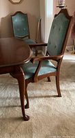 Close-up of table corner and one armchair showing cherry wood finish and green upholstery