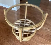 Full view of round rattan table with glass top on hardwood floor.